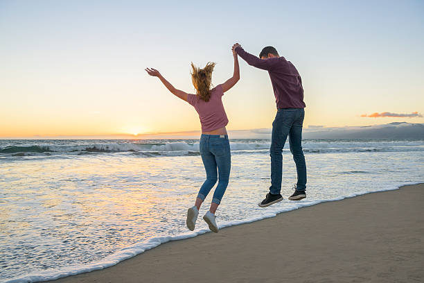 istock Young couple holding hands and jumping on beach 629604888