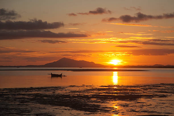 Looking from the port town of Ankify, a beautiful sunrise glows over local fisherman's  beached canoes at low tide with mountains, the Madagascar mainland and islands in the distance in the Mozambique Channel part of the Indian Ocean.