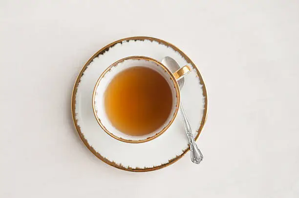 An old fashioned (vintage) cup of tea and a silver spoon on a white background taken from directly above. 