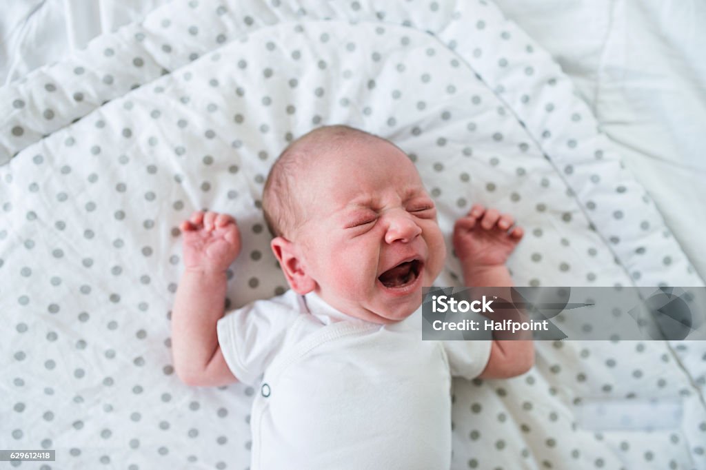 Newborn baby boy lying on bed, crying, close up Cute little newborn baby boy lying on bed, crying. Close up. Baby - Human Age Stock Photo