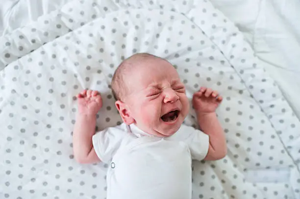 Cute little newborn baby boy lying on bed, crying. Close up.