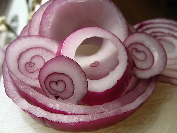 A raw red onion sliced many times revealing naturally found heart shapes in the center of each slice