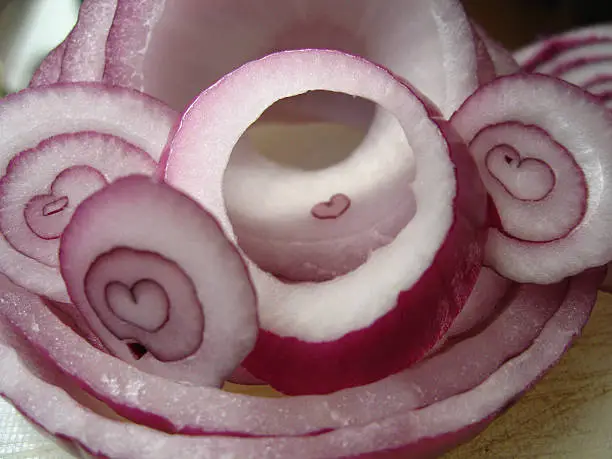 A raw red onion sliced many times revealing naturally found heart shapes in the center of each slice