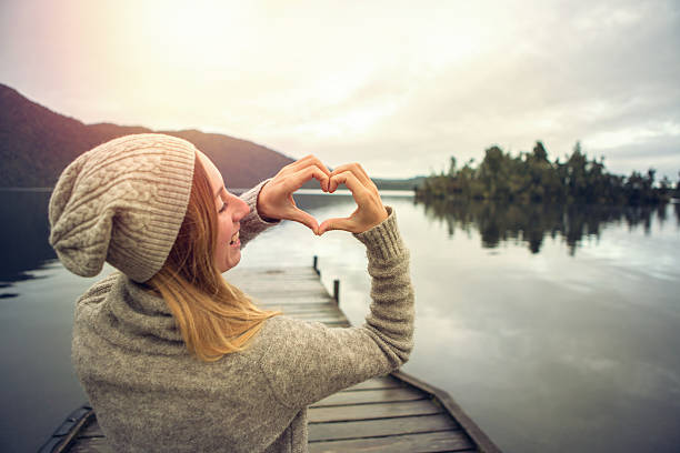 Young woman on lake pier, makes heart shape finger frame