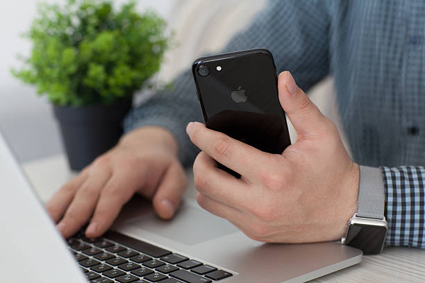 Alushta, Russia - November 2, 2016: Man hand with Apple Watch holding iPhone 7 Jet Black over Macbook Pro. iPhone 7 was created and developed by the Apple inc.