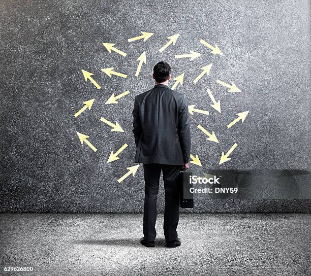 Businessman Looking At Arrows Pointing In Different Directions Stock Photo - Download Image Now