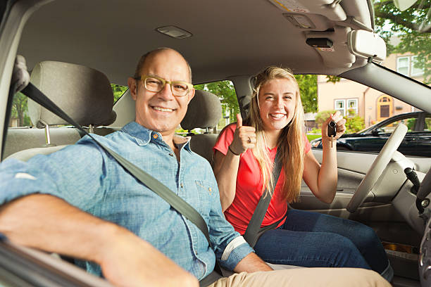 Parent Driving Instructor and Happy Teenage Student Driver in Car A happy teenager young woman receiving a new car from her parent father. The young woman is holding the key to the car and they are smiling and posing for the camera inside their new car.  driving test photos stock pictures, royalty-free photos & images