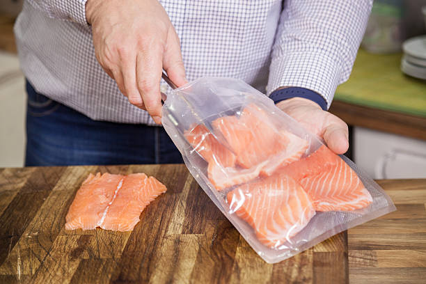 Packing salmon for sous vide. Man putting salmon fillets into a plastic bag and making preparations for sous vide cooking. vacuum packed stock pictures, royalty-free photos & images