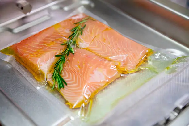 Salmon in olive oil and rosemary on vacuum seal machine. Sous vide.