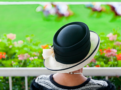 A fashionable lady dressed for the occasion in classic black and white at the racecourse watching the thoroughbred race horses race on turf at the racecourse, on a late summer’s day.