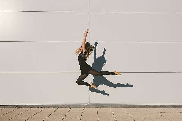 Elegant female ballet dancer performing in front of building wall Elegant, attractive ballerina performing outdoor in front of building wall, jumping high. Copy space composition. Photo is taken with dslr camera on sunny autumn day in Europe. ballerina shadow stock pictures, royalty-free photos & images