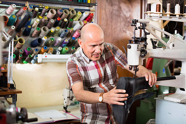 Mature workman sewing leather boots on stitch lathe