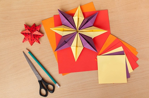 Handmade paper stars, scissors, pencil and color paper on wooden table, background.