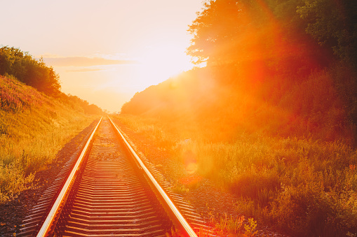 The Scenic Landscape With Railway Going Straight Ahead Through Summer Hilly Meadow To Sunset Or Sunrise In Sunlight. Lense Flare Effect.