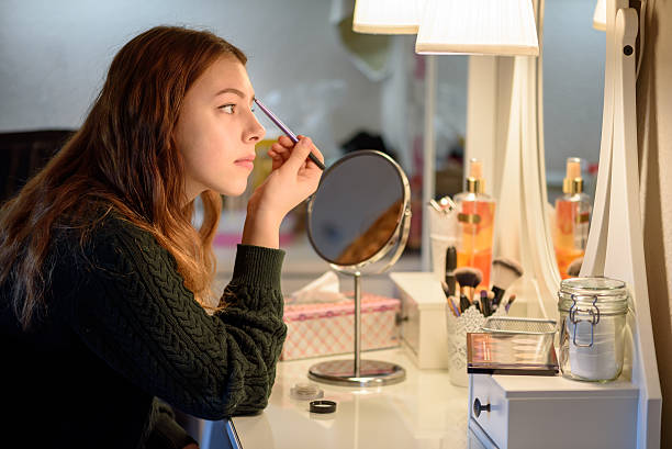 Applying makeup Young woman applying makeup cosmetics in front of a mirror at home ceremonial make up stock pictures, royalty-free photos & images