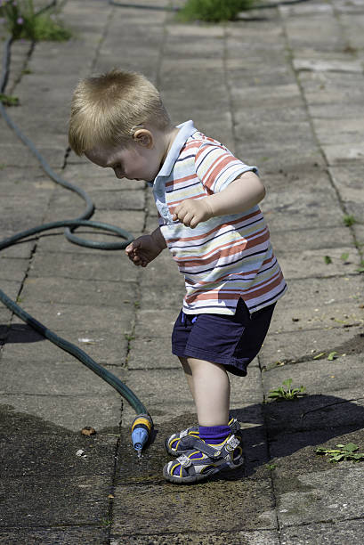 istock Boy with hearing aid plays with water hose 629666868