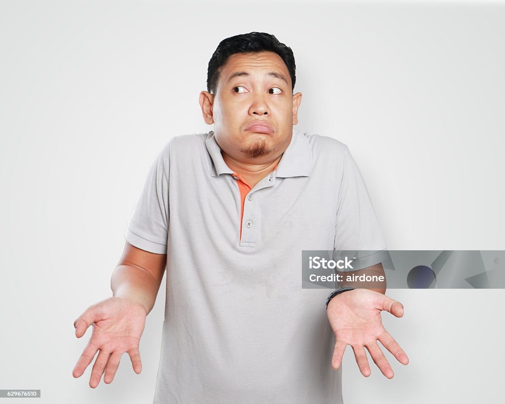 Funny Young Asian Guy Shrug Gesture Photo image portrait of a cute young Asian man showing I don't know gesture, shoulder shrug and looking to the side Men Stock Photo