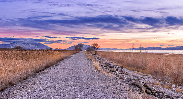 Dusk at Utah Lake A gravel path runs along the side of Utah Lake, trailing off into the distance as dusk settles coloring the sky with the after glow of the sunset. lake utah stock pictures, royalty-free photos & images