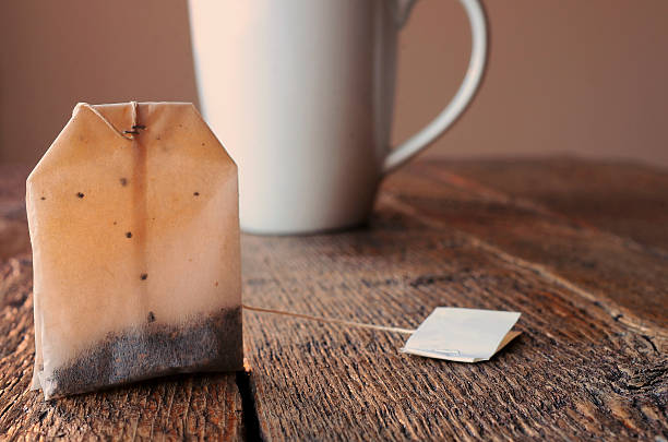Teabag and Teacup A close up image of a rectangular teabag with a white teacup in the background.  decaffeinated photos stock pictures, royalty-free photos & images