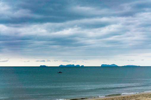 An unrecognizable man kayaks on the Andaman Sea, Krabi, Thailand.  The sky above is dark and moody, a storm is brewing.  On the horizon the Phi Phi Islands can be seen.