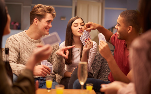 a group of young friends sit on the sofa and play a game of cards . There are drinks on the table too where it could be a drinking game .