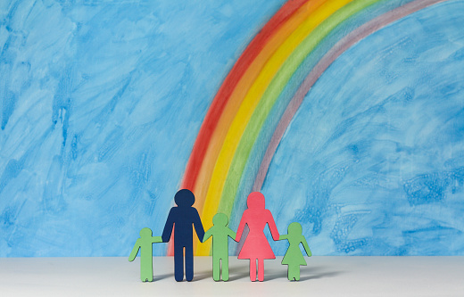 Father, mother and children icons with a rainbow and blue sky to illustrate the concept of the traditional family unit in landscape format.