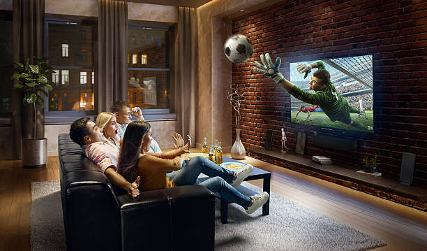 Couples watching very realistic Soccer game on TV :biggrin:A group of young friends are shocked while watching Soccer game on TV. They are sitting on a sofa in the modern living room. The TV set is on the loft brick wall. It is evening outside the window. excited football fan cheering for his team on tv stock pictures, royalty-free photos & images