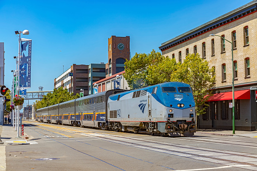 Oakland, United States - August 3, 2016: Amtrak California train service proceeds slowly down Embarcadero West past the clock tower, approaching Jack London Square Station, Oakland, California.  