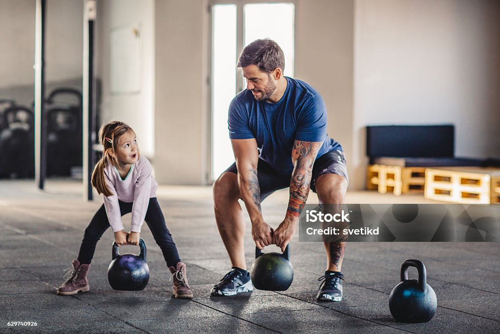 She's gonna be strong like daddy Father doing his training with kettlebells in gym while his little daughter supporting him. Father Stock Photo