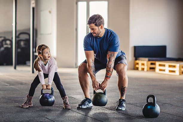 She's gonna be strong like daddy Father doing his training with kettlebells in gym while his little daughter supporting him. professional sportsperson stock pictures, royalty-free photos & images