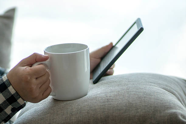 istock drinking coffee and reading ebook on sofa beside window 629742240