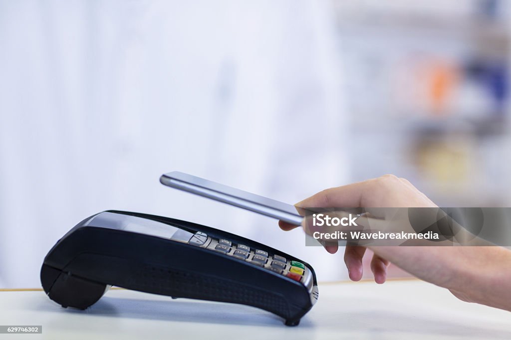 Woman paying bill through smartphone using NFC technology Woman paying bill through smartphone using NFC technology in pharmacy Mobile Payment Stock Photo