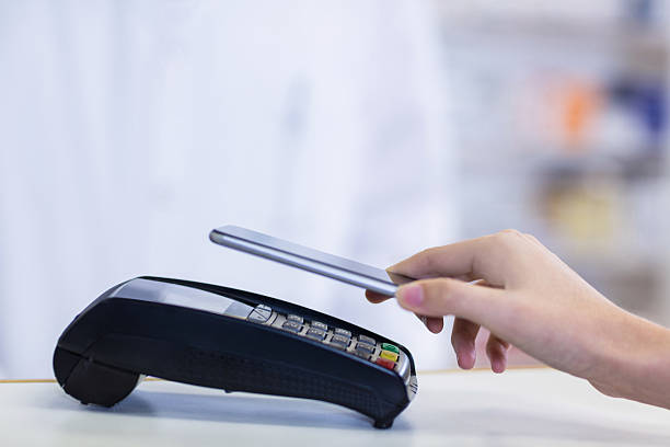 Woman paying bill through smartphone using NFC technology Woman paying bill through smartphone using NFC technology in pharmacy mobile payment photos stock pictures, royalty-free photos & images