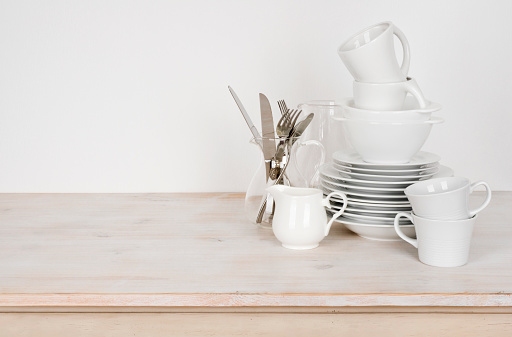 White dishware and cutlery on wooden table with copy space