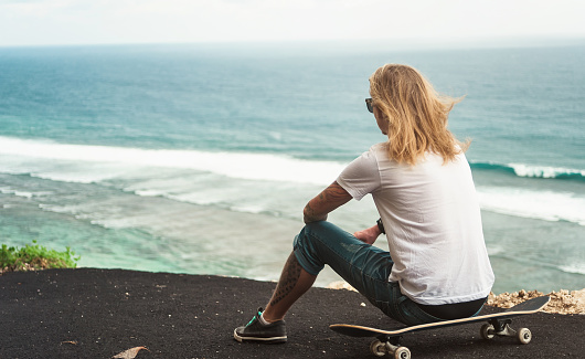 Young man blonde skater sitting in front of amazing ocean view