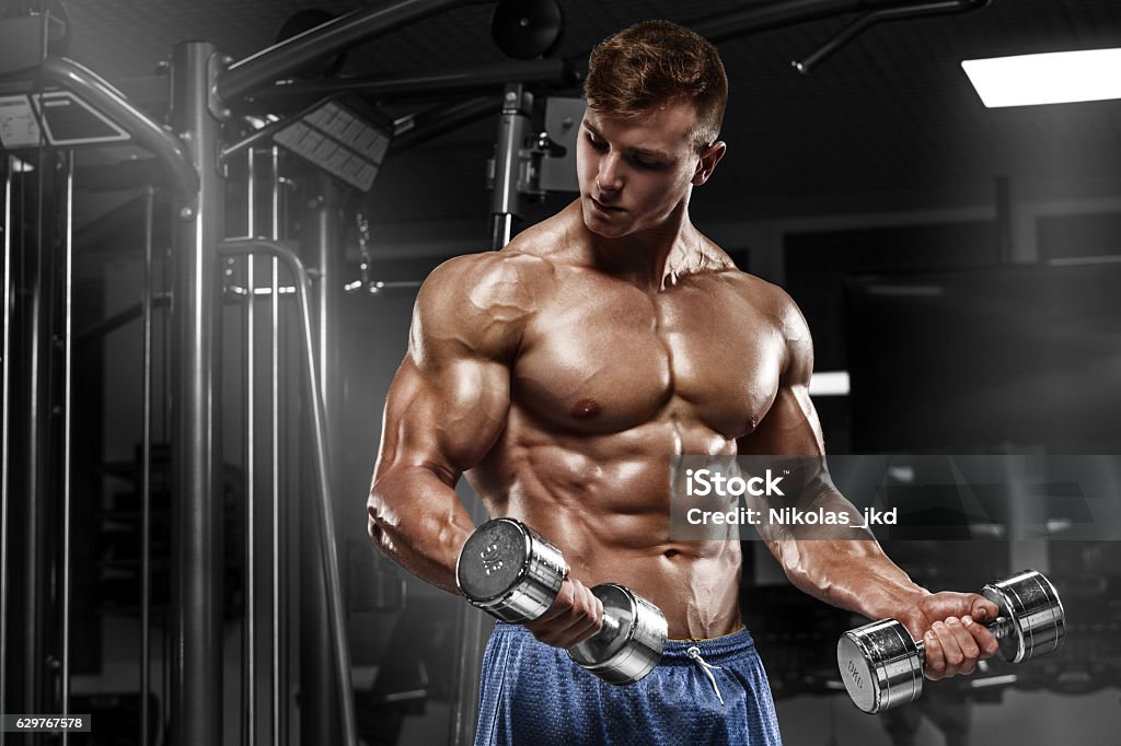 Muscular man working out in gym doing exercises, torso abs Muscular man working out in gym doing exercises with dumbbells at biceps, strong male naked torso abs Macho Stock Photo
