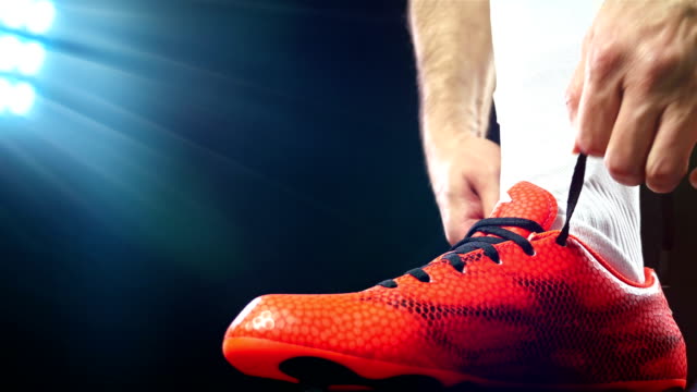 Football, soccer game. Professional footballer buckle his red shoes, black background