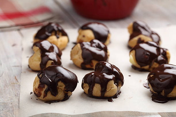 Profiteroles glazed with chocolate Rows of Profiteroles with chocolate glaze on a baking paper choux pastry photos stock pictures, royalty-free photos & images