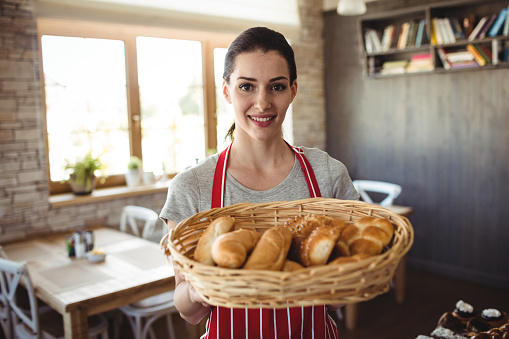 Portrait of female baker holding a basket of bread loafs in bakery shop
