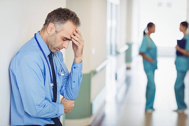 Serious male healthcare worker standing in front of hospital and looking at camera.