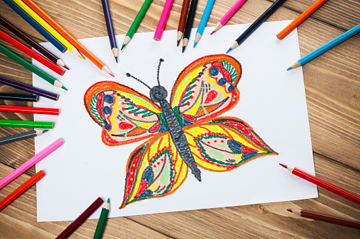 Children's drawings on white  paper with  colorful pencils on the wooden table