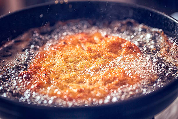 frying wiener schnitzel in deep oil in a cooking pan - viennese schnitzel imagens e fotografias de stock
