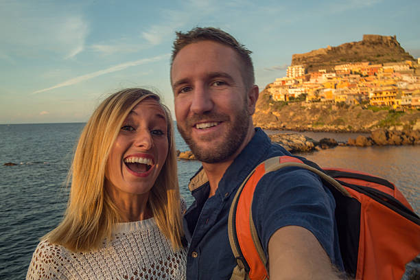 Young couple in Italy take a selfie portrait Young couple in Italy take a selfie portrait with Castelsardo village and seascape on the background. Sunset light, late summer day. castelsardo photos stock pictures, royalty-free photos & images