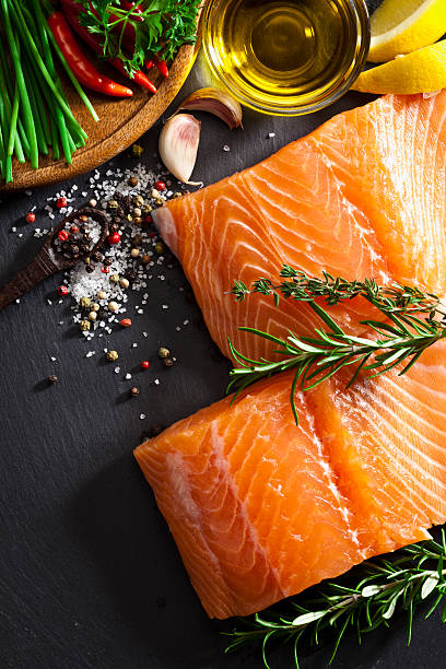 Raw salmon steak Two raw salmon steaks shot from above on dark stone background. Some ingredients for cooking salmon like lime, salt, pepper, garlic, chive, rosemary and olive oil are visible at the upper side of the frame. DSRL studio photo taken with Canon EOS 5D Mk II and Canon EF 100mm f/2.8L Macro IS USM salmon stock pictures, royalty-free photos & images