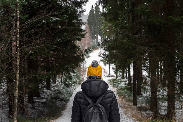 walk in winter forest alone young woman in black down jacket and yellow knitted hat with rucksack in the depth of the black forest during cold winter day in finland snow hiking stock pictures, royalty-free photos & images