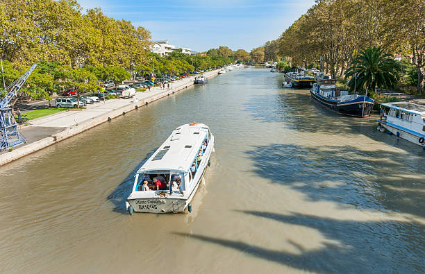 Beziers France - September 24, 2016: River boats moored along Canal Du Midi as  Monto Dabalo with tourist passengers passes along after crossing Orb Aqueduct in Beziers, France