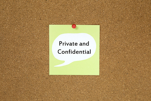 The phrase private and confidential on a green sticky note posted to a cork notice board