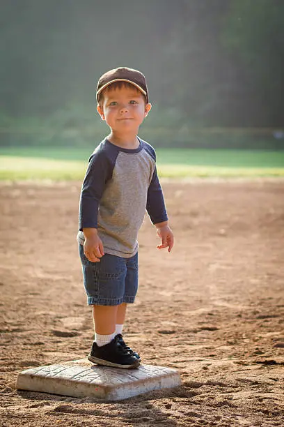 A young boy stands on second base.  He is looking into the camera.