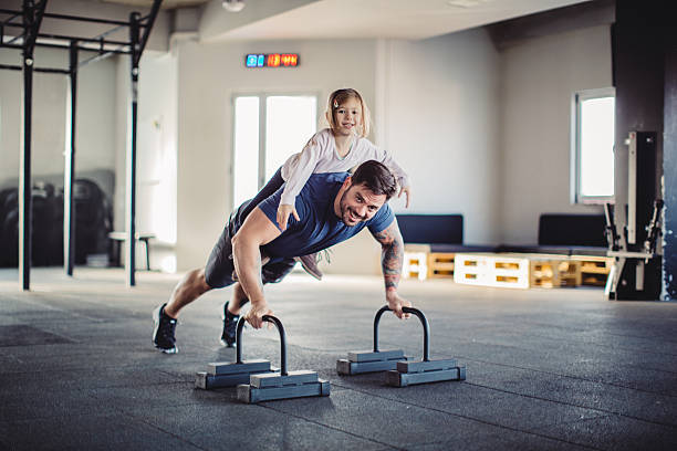 Everything is funnier with her Father doing his training in gym with little daughter on his back. crossfit girl stock pictures, royalty-free photos & images