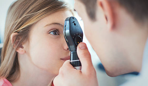 At optician's office. Closeup side view of early 40's unrecognizable optician examining eyesight of his little female patient with a phoropter device. The girls is aged 9, with brown eyes and hair. eye test equipment stock pictures, royalty-free photos & images